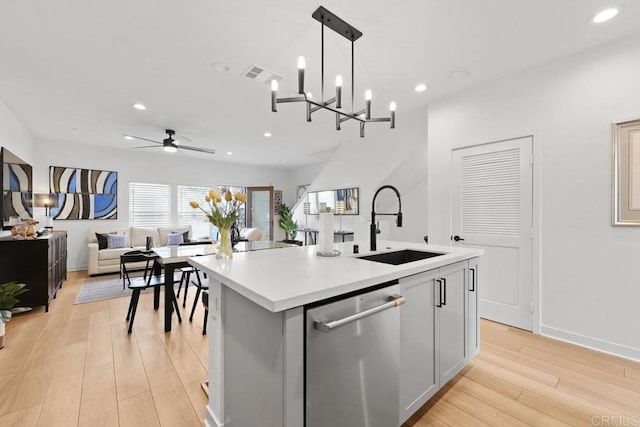 kitchen with sink, a kitchen island with sink, hanging light fixtures, light hardwood / wood-style floors, and stainless steel dishwasher