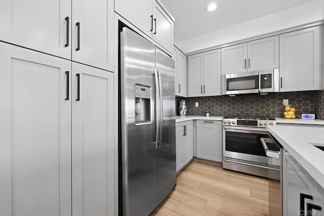 kitchen with stainless steel appliances, tasteful backsplash, gray cabinetry, and light wood-type flooring