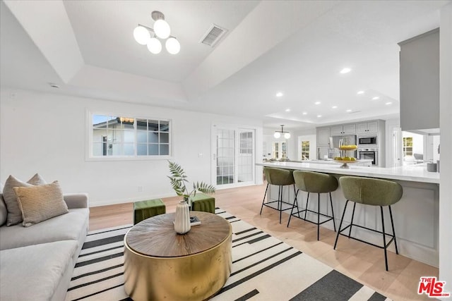 living room with a tray ceiling, a chandelier, and light hardwood / wood-style floors