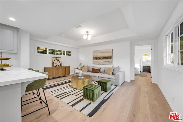 living room with a raised ceiling, a healthy amount of sunlight, and light hardwood / wood-style flooring