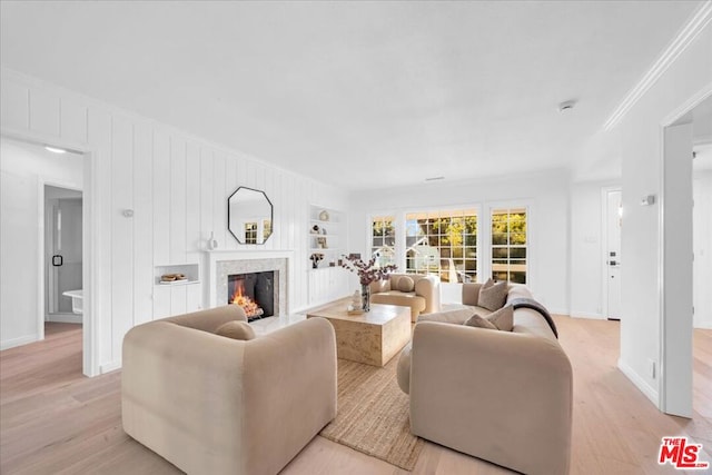 living room with crown molding, light wood-type flooring, a fireplace, and built in shelves