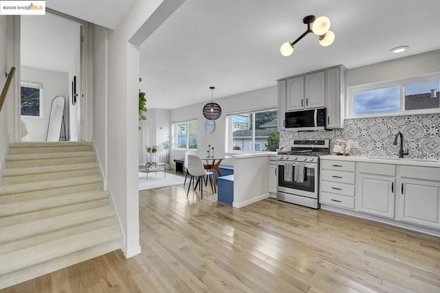 kitchen with appliances with stainless steel finishes, tasteful backsplash, sink, hanging light fixtures, and light hardwood / wood-style flooring