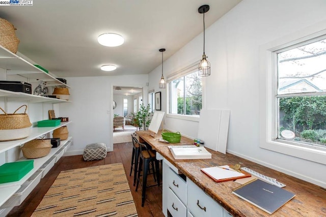 interior space featuring white cabinetry, dark hardwood / wood-style floors, pendant lighting, and a kitchen bar