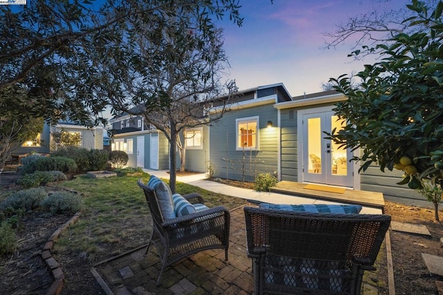 back house at dusk featuring french doors and a patio