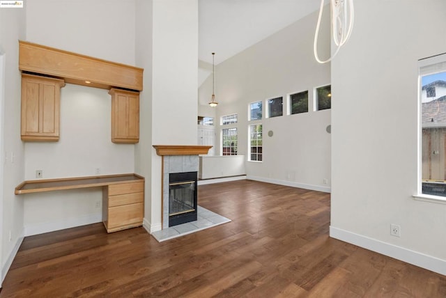 unfurnished living room featuring a tiled fireplace, dark hardwood / wood-style floors, built in desk, and a towering ceiling