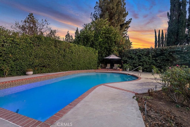 pool at dusk featuring a gazebo and a patio