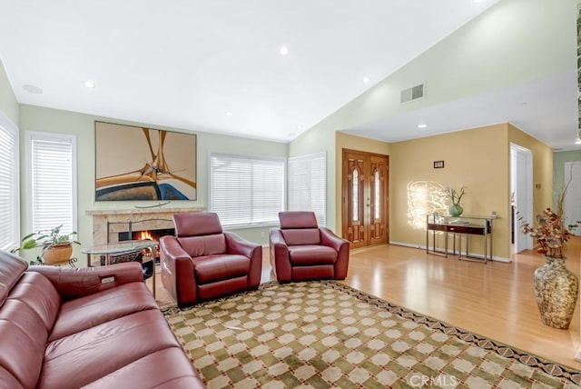 living room featuring a high end fireplace, high vaulted ceiling, light hardwood / wood-style flooring, and a wealth of natural light