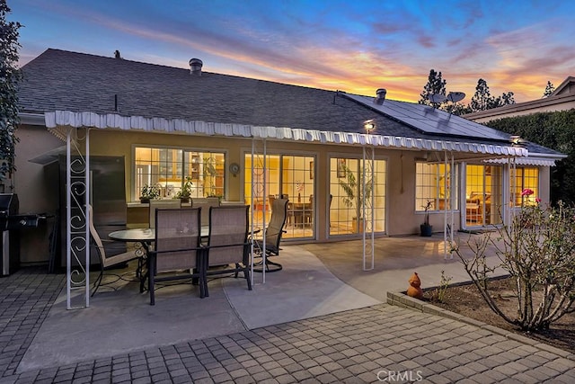 back house at dusk with a patio and solar panels