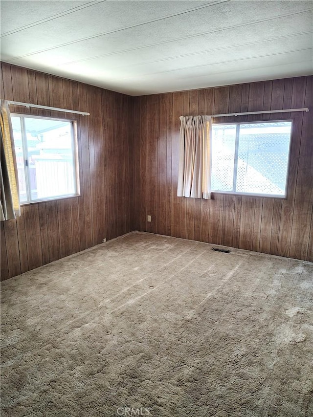 carpeted spare room with visible vents and wooden walls