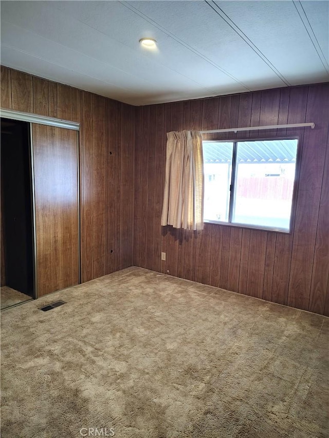 empty room featuring carpet flooring, visible vents, and wooden walls