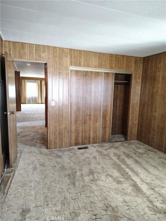 empty room featuring visible vents, light colored carpet, and wooden walls