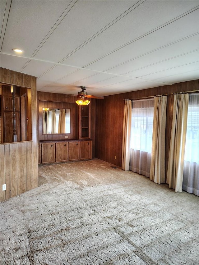 empty room featuring light carpet, ceiling fan, and wooden walls