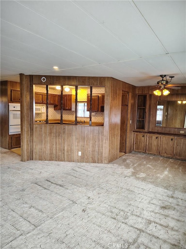 interior space with carpet, wooden walls, and a ceiling fan