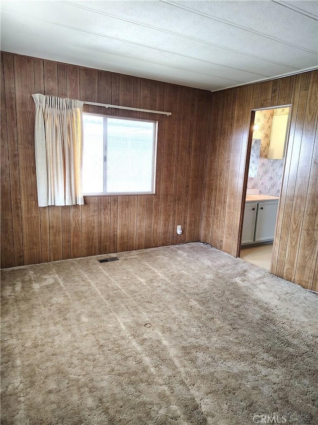 spare room with visible vents, light carpet, and wooden walls