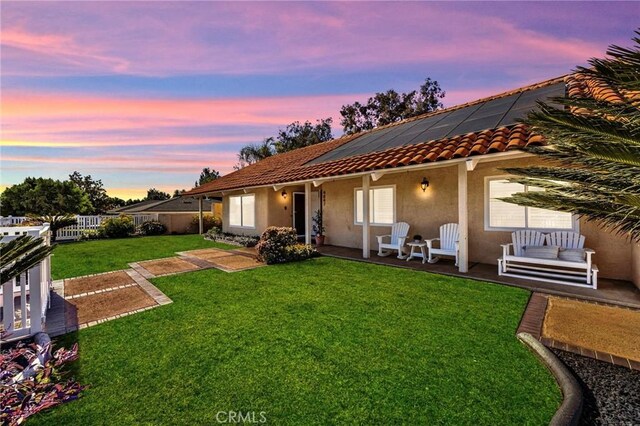 back house at dusk featuring a yard and solar panels