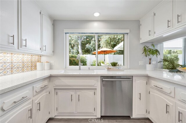 kitchen with sink, white cabinets, backsplash, stainless steel dishwasher, and light stone countertops