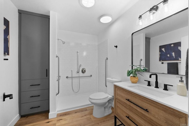 bathroom featuring toilet, a tile shower, wood finished floors, and vanity