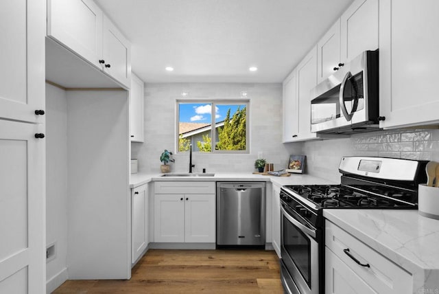 kitchen with white cabinets, decorative backsplash, stainless steel appliances, light wood-type flooring, and a sink