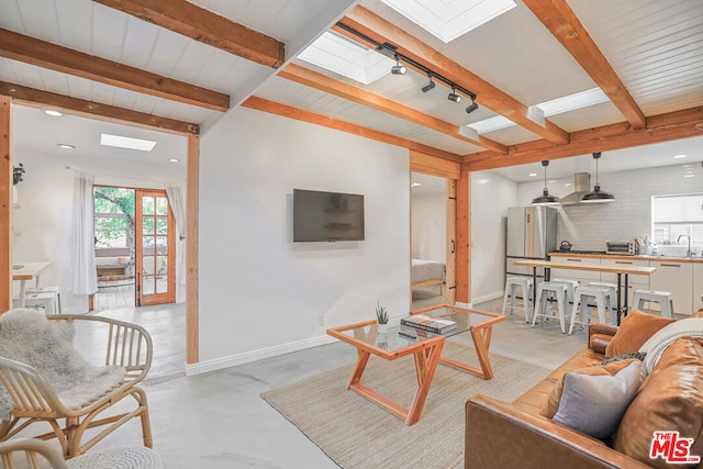 living room featuring sink, track lighting, beam ceiling, and a skylight