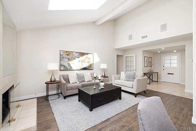 living room featuring hardwood / wood-style floors, a skylight, beamed ceiling, and a brick fireplace