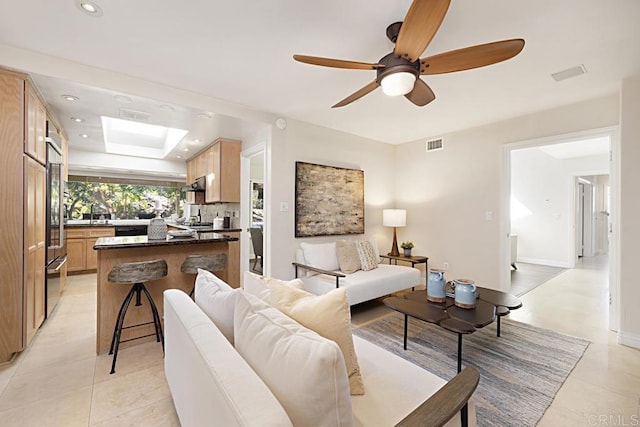 tiled living room with ceiling fan and a skylight