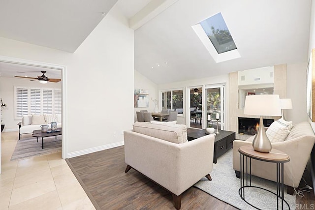 living room with a skylight, high vaulted ceiling, beam ceiling, a tiled fireplace, and tile patterned flooring