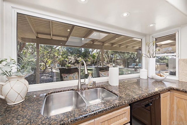 kitchen featuring dark stone counters, black dishwasher, sink, and light brown cabinets