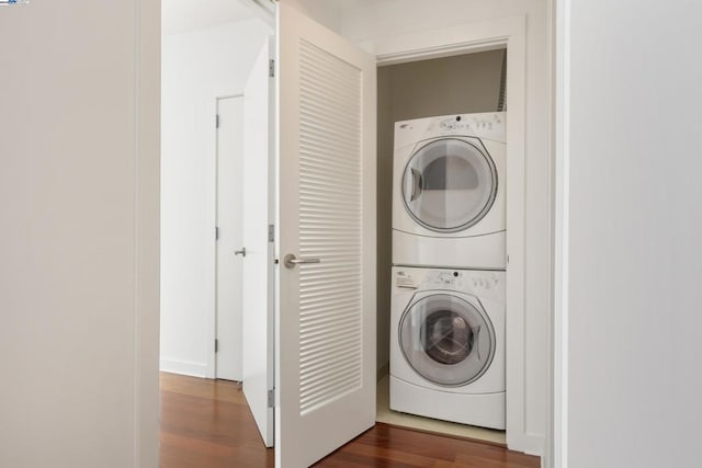 washroom with stacked washer / drying machine and dark hardwood / wood-style flooring