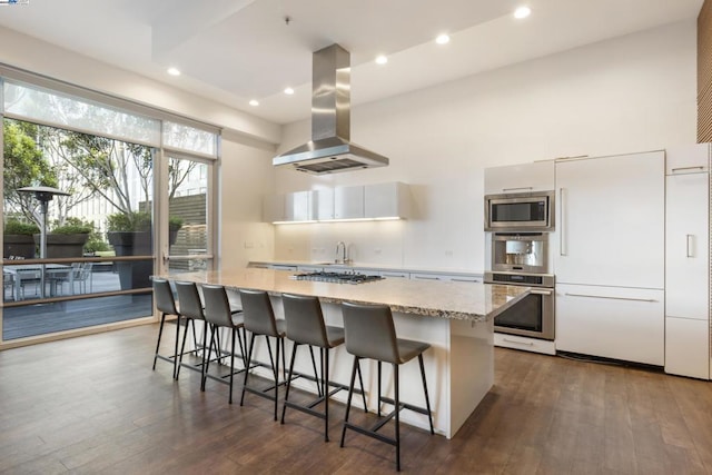 kitchen featuring a kitchen breakfast bar, a center island, built in appliances, white cabinets, and island exhaust hood