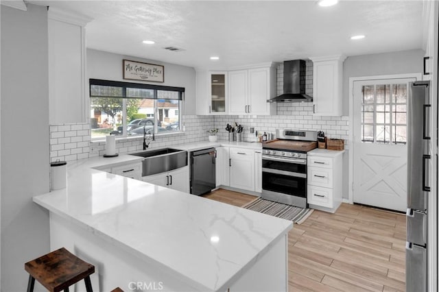 kitchen featuring appliances with stainless steel finishes, kitchen peninsula, white cabinets, and wall chimney exhaust hood