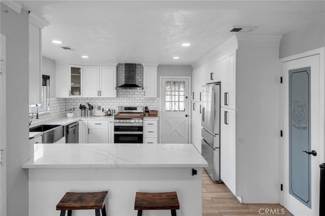 kitchen featuring wall chimney exhaust hood, a breakfast bar, sink, appliances with stainless steel finishes, and kitchen peninsula