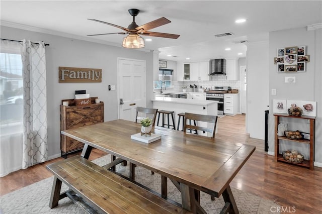 dining room with ornamental molding, sink, and light hardwood / wood-style floors