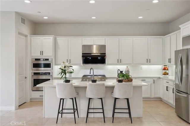 kitchen featuring white cabinetry, decorative backsplash, a center island with sink, and appliances with stainless steel finishes