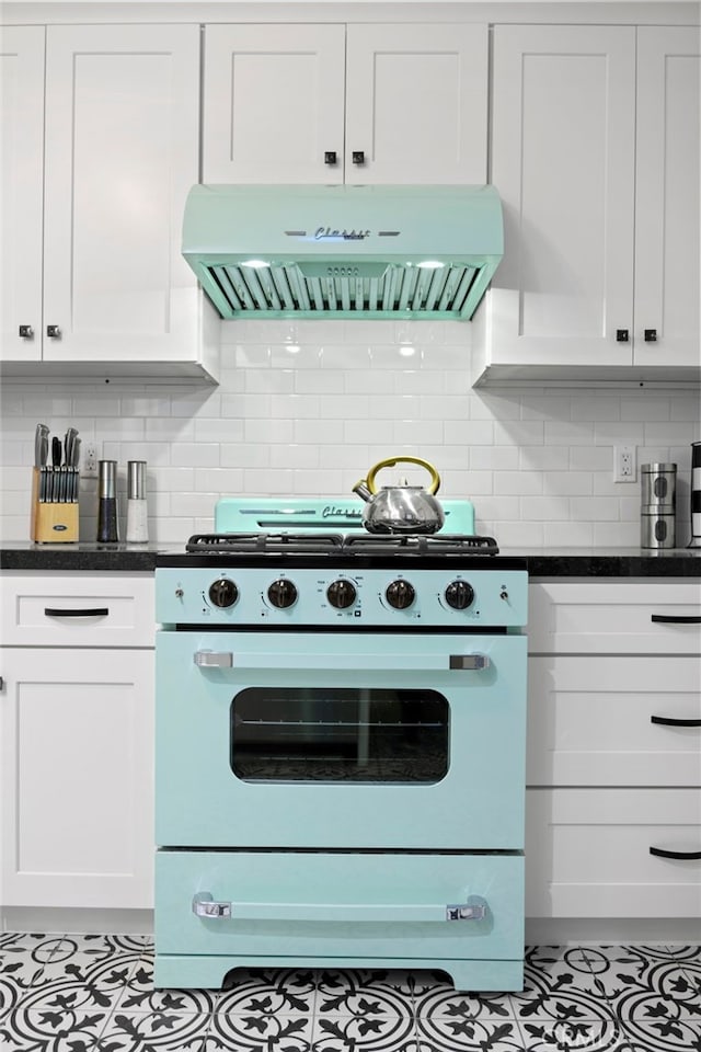 kitchen featuring stove, tasteful backsplash, range hood, and white cabinets