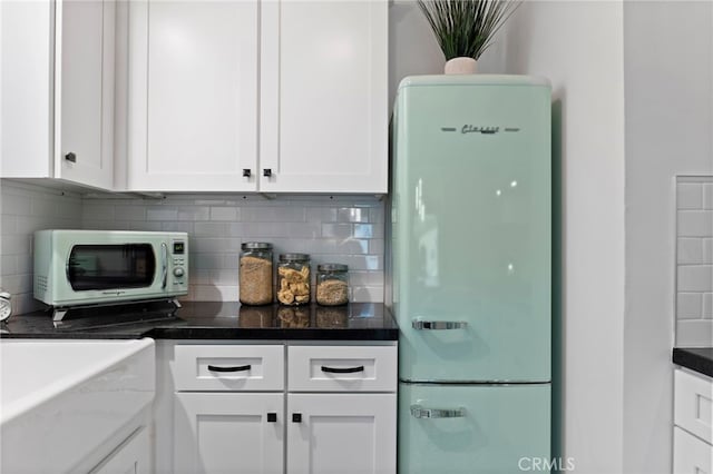 kitchen featuring white cabinetry, decorative backsplash, dark stone countertops, and white fridge