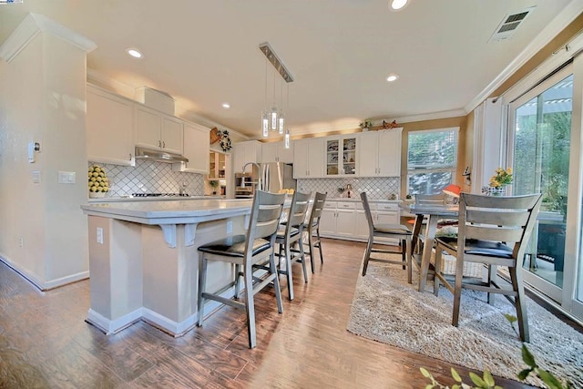 kitchen featuring a kitchen island, stainless steel refrigerator, white cabinetry, hanging light fixtures, and ornamental molding