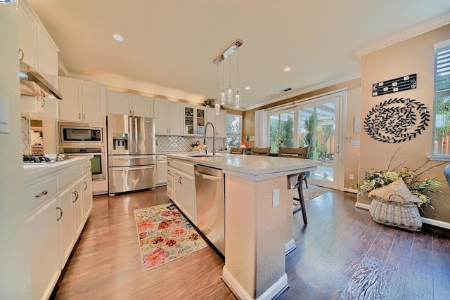 kitchen featuring appliances with stainless steel finishes, a breakfast bar, pendant lighting, white cabinetry, and a center island with sink