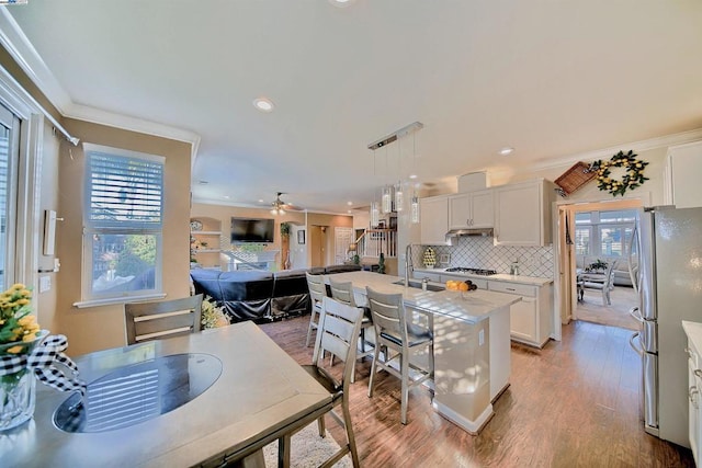 kitchen with pendant lighting, crown molding, a kitchen island with sink, and white cabinets