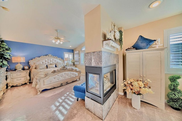 bedroom with a tiled fireplace, light colored carpet, ceiling fan, and lofted ceiling