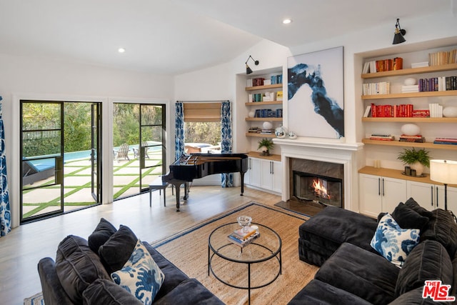 living room featuring lofted ceiling, built in features, a premium fireplace, and light wood-type flooring