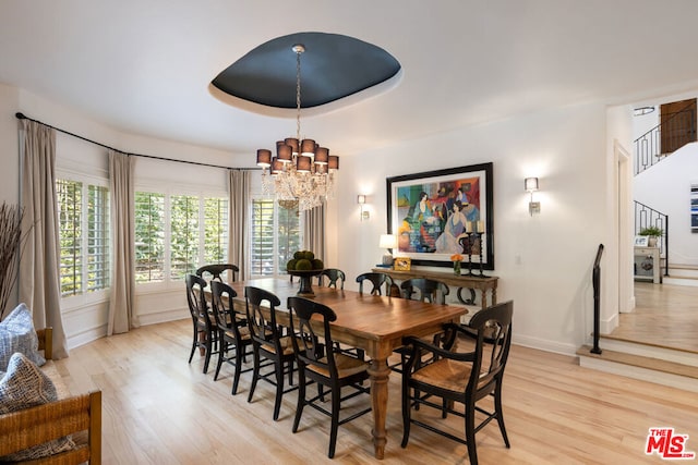 dining space with an inviting chandelier, light hardwood / wood-style floors, and a raised ceiling