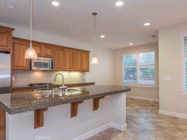 kitchen with pendant lighting, tasteful backsplash, sink, a kitchen island with sink, and stainless steel appliances