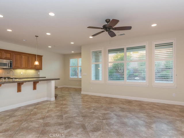 kitchen with a kitchen bar, sink, light stone counters, pendant lighting, and ceiling fan