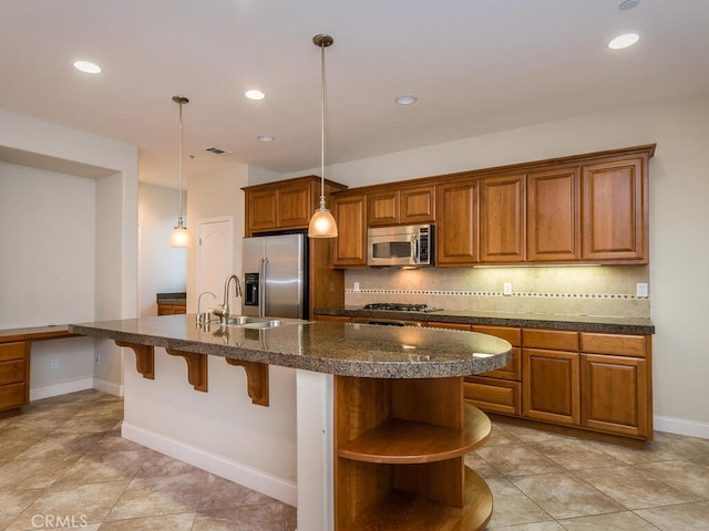 kitchen with tasteful backsplash, stainless steel appliances, decorative light fixtures, and a kitchen island with sink