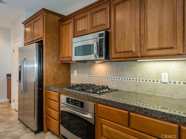 kitchen with stainless steel appliances, dark stone counters, decorative backsplash, and light tile patterned floors