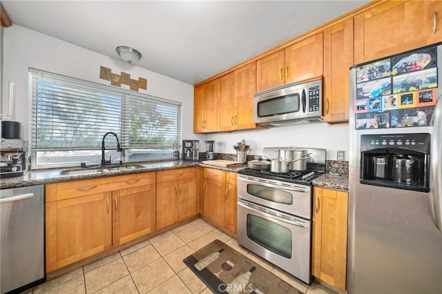 kitchen featuring appliances with stainless steel finishes, sink, light tile patterned floors, and dark stone counters