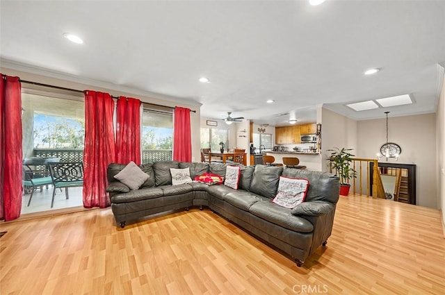 living room featuring ornamental molding, a skylight, ceiling fan with notable chandelier, and light hardwood / wood-style flooring