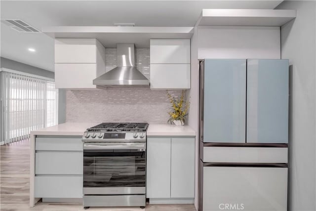 kitchen featuring white cabinetry, backsplash, fridge, gas range, and wall chimney exhaust hood