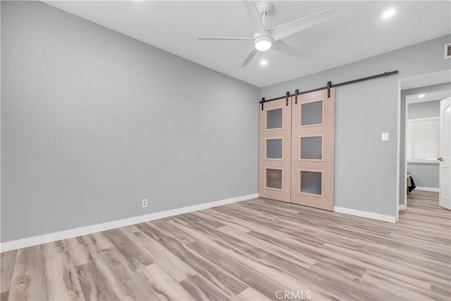 unfurnished bedroom with light hardwood / wood-style floors, a barn door, and ceiling fan