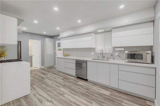 kitchen with sink, stainless steel appliances, tasteful backsplash, white cabinets, and light wood-type flooring